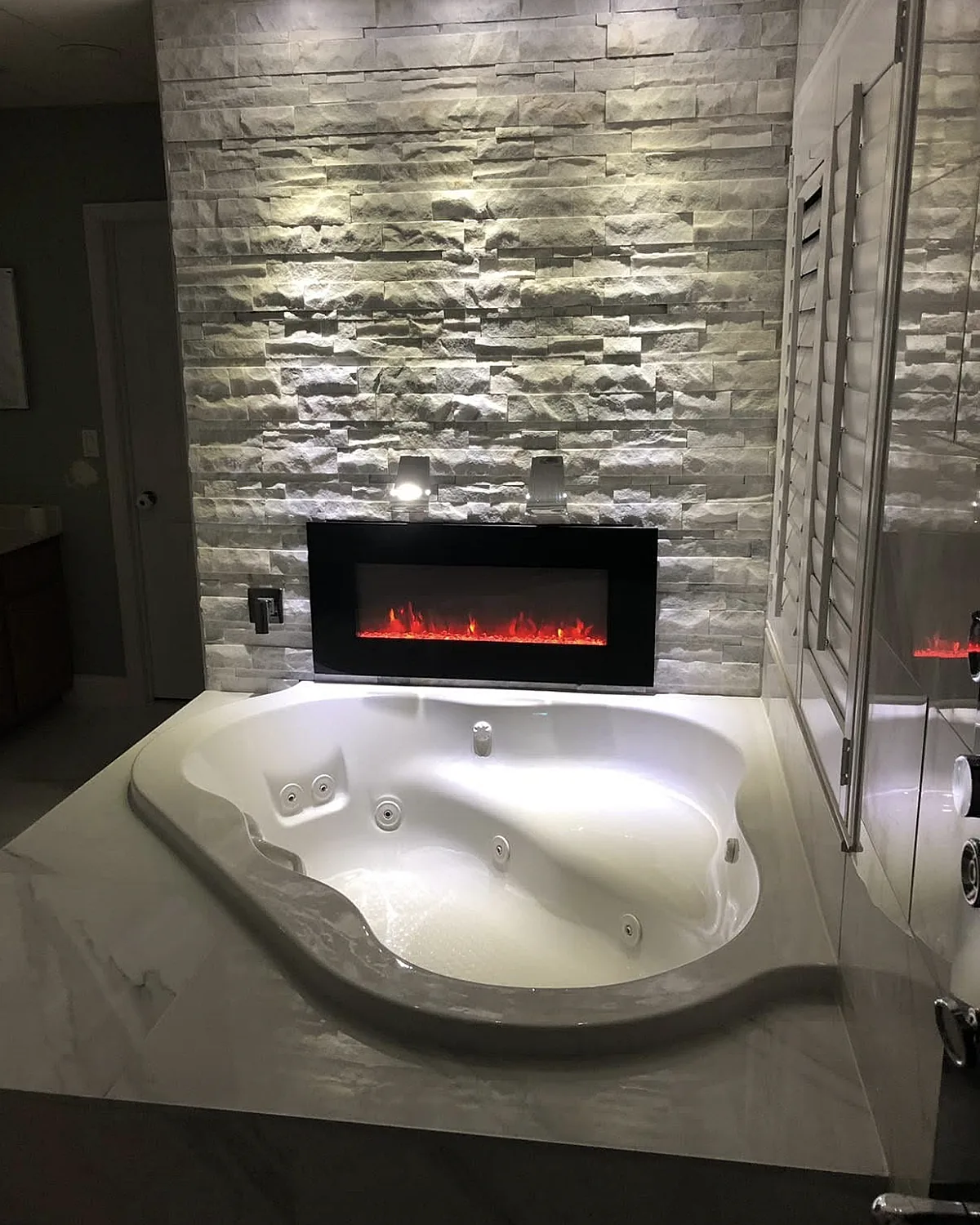 Spa tub with a fireplace and stone accent wall